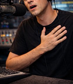 Young radio host struggling to breathe during live broadcast in studio while speaking into microphone